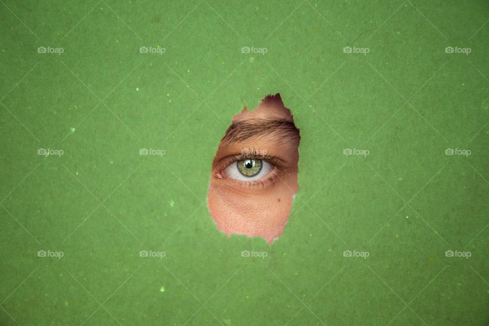 Human eye looking through green torn paper.