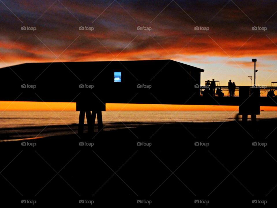 People on the fishing pier over the Gulf of Mexico are enjoying each other and taking in the magnificent and colorful sunset. The awesome beauty of the setting sun and reflecting off the multi-colored clouds