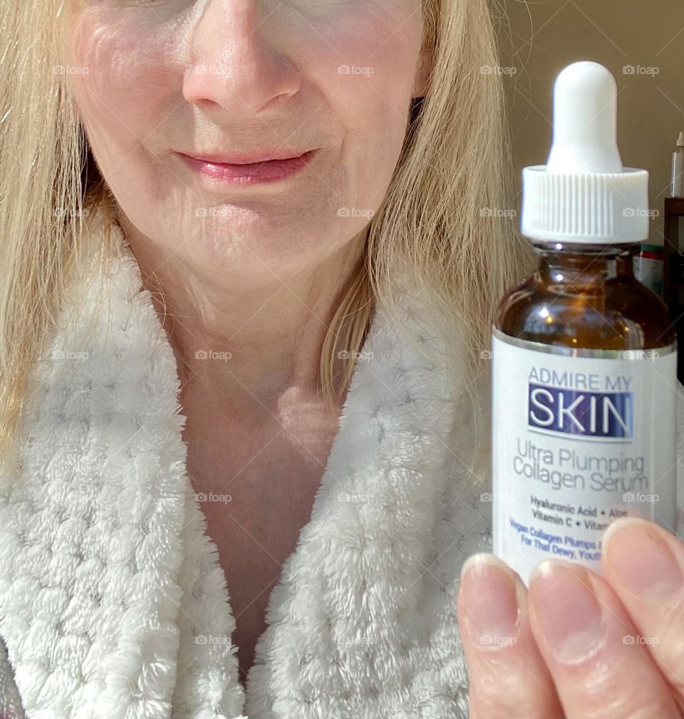 Woman in bathrobe holding a skincare product 