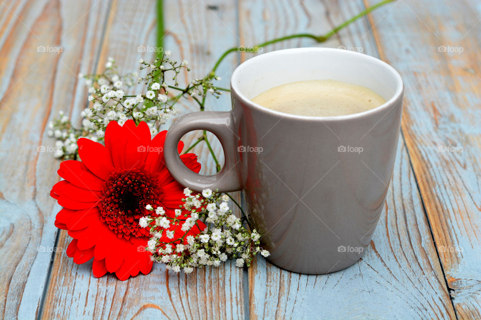 cup of coffee on a wooden table background with red daisy flower