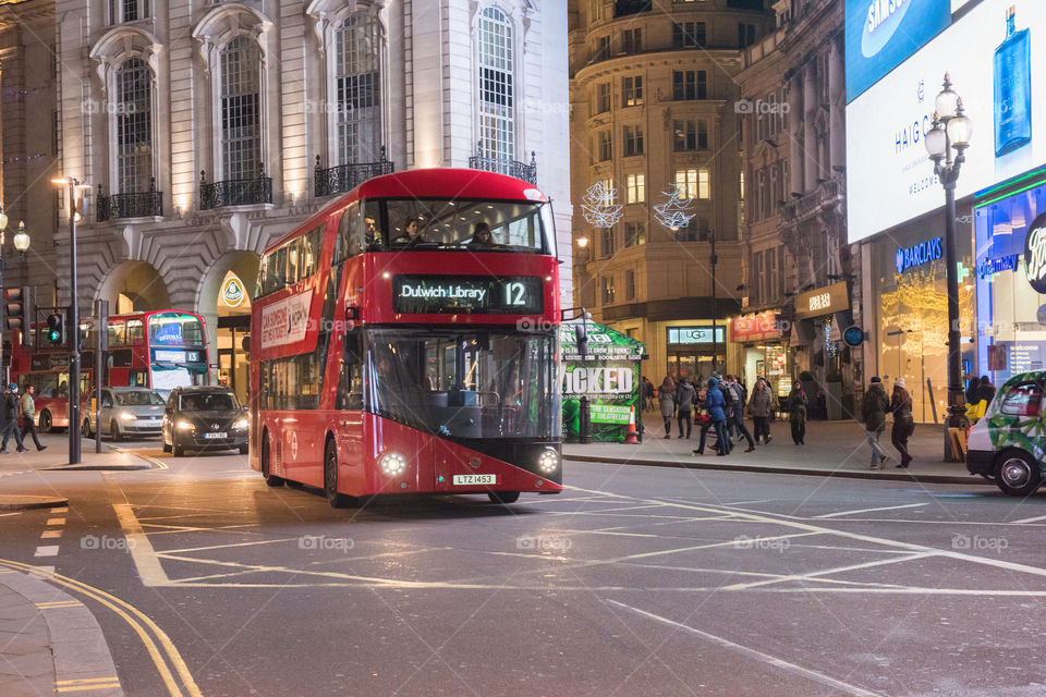 A red London bus driving past Piccadilly Circus in London in the evening.