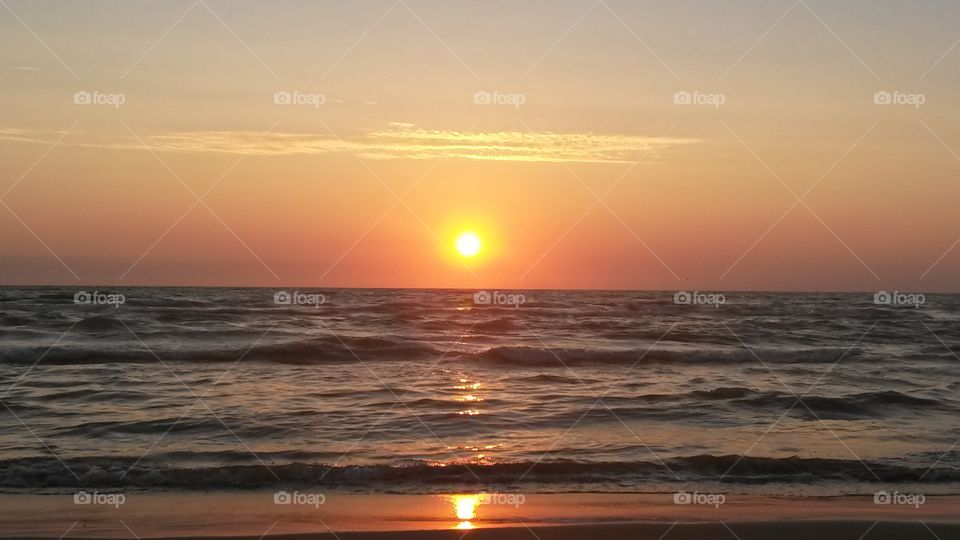 yellow red sunset at the beach with ocean and sun reflection on the water and sand