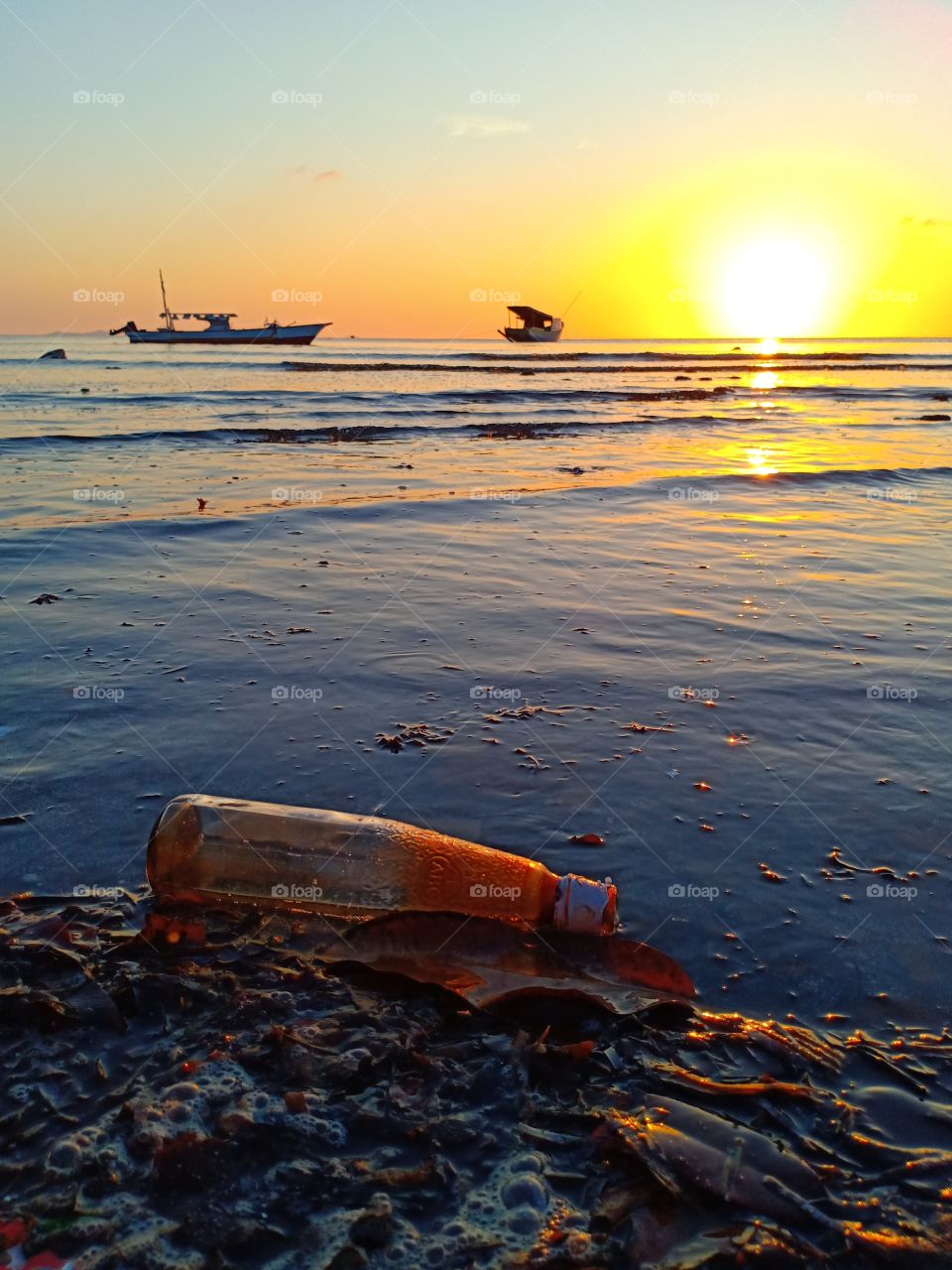 an abandoned glass bottle on the beach and beautiful gold colorful sunset. keep the beach clean will save the marine life.