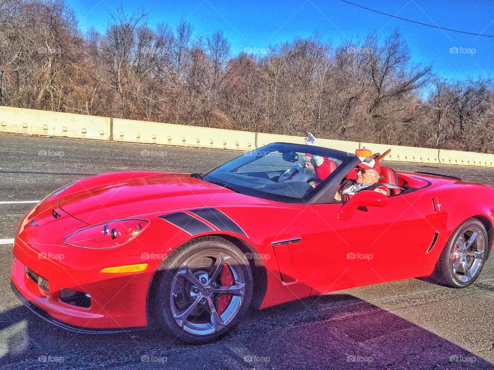 Senior man sitting in red car with santa clause