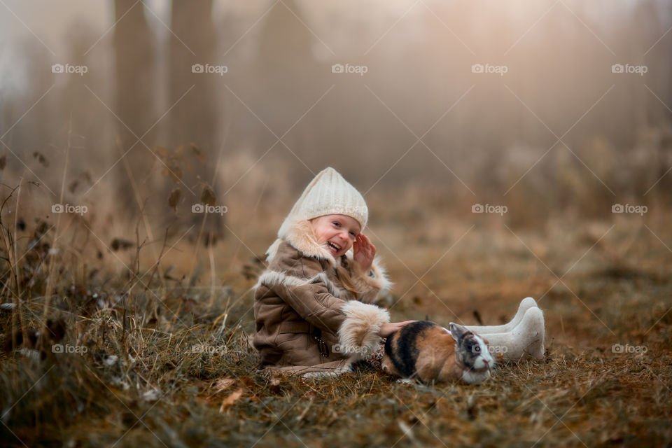 Cute Little girl with bunny in a forest at misty autumn evening 