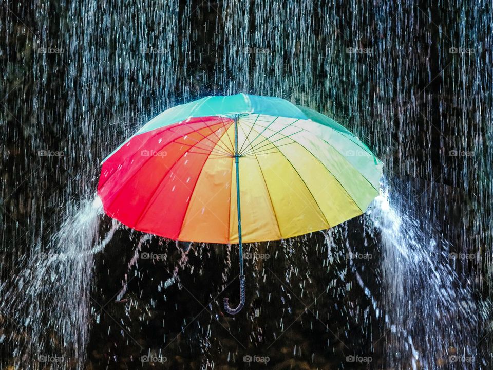 A suspended colorful umbrella under the pouring monsoon rain in Kuala Lumpur at night