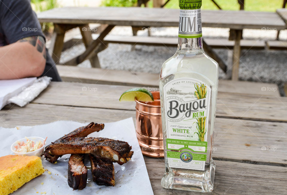 Bottle of Bayou white rum next to a copper mug and smoked ribs on a wooden table
