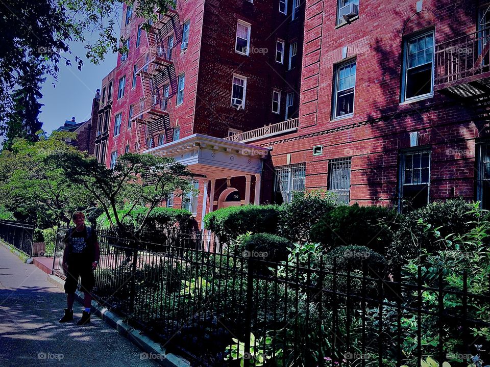 View of one of many old fashioned style brownstone buildings in Fort Greene, Bklyn with unusual details like arched windows, towers, columns, stucco ornaments and artwork, iron cast fences and beautifully kept greenery. 2020. Hypnotic Productions