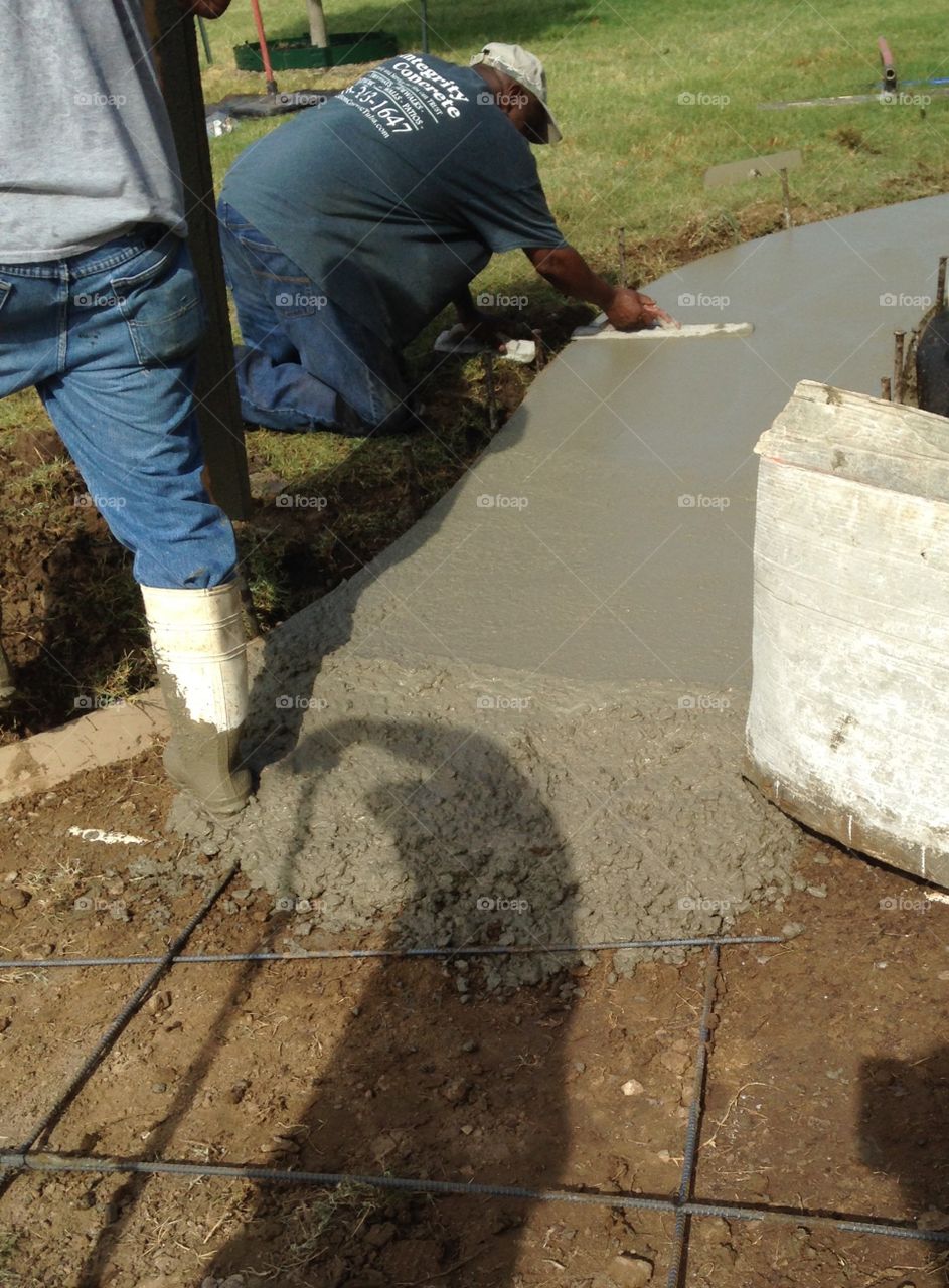Man on hands and knees leveling wet concrete using tools