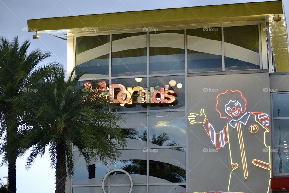 Exterior of the World’s Largest McDonalds featuring a neon display of Ronald McDonald, glass windows, and palm trees. 