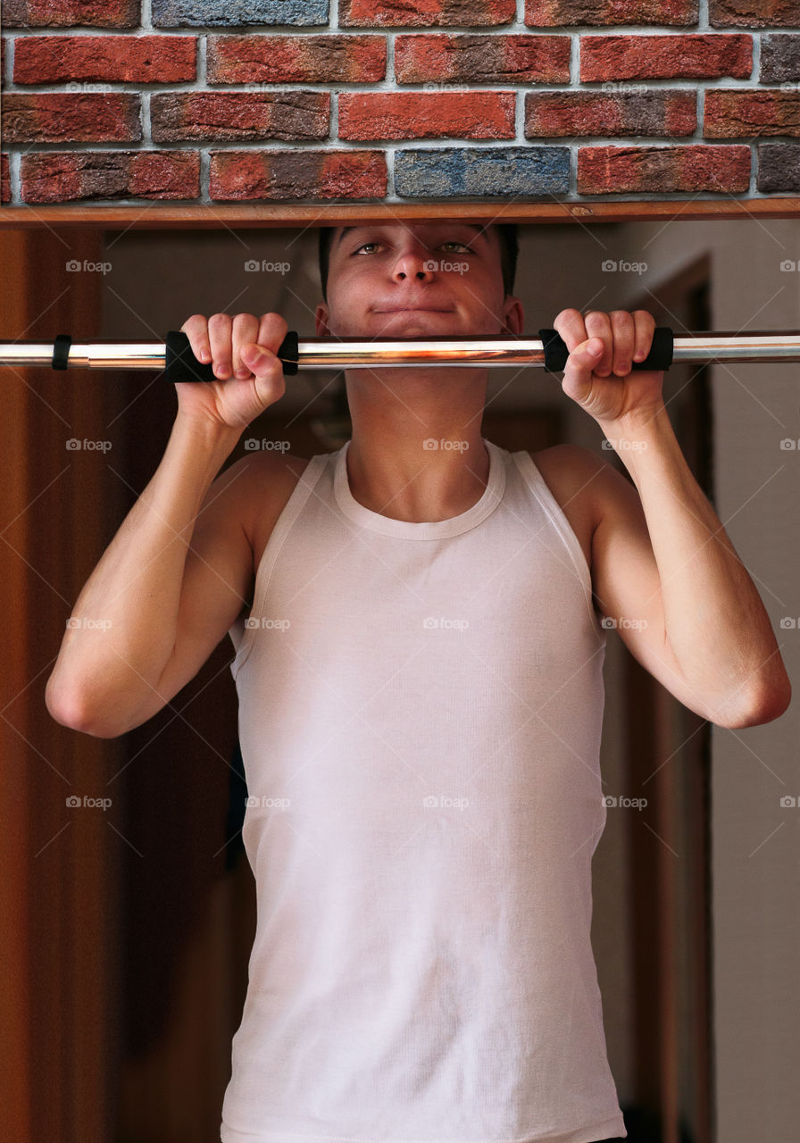 Young man executing exercise pulling up on horizontal bar at home. Portrait orientation