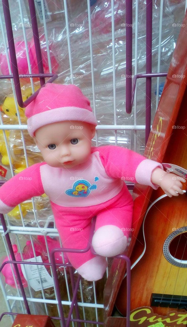 Baby doll dressed in pink suit is sitting on a trolley in the toy store