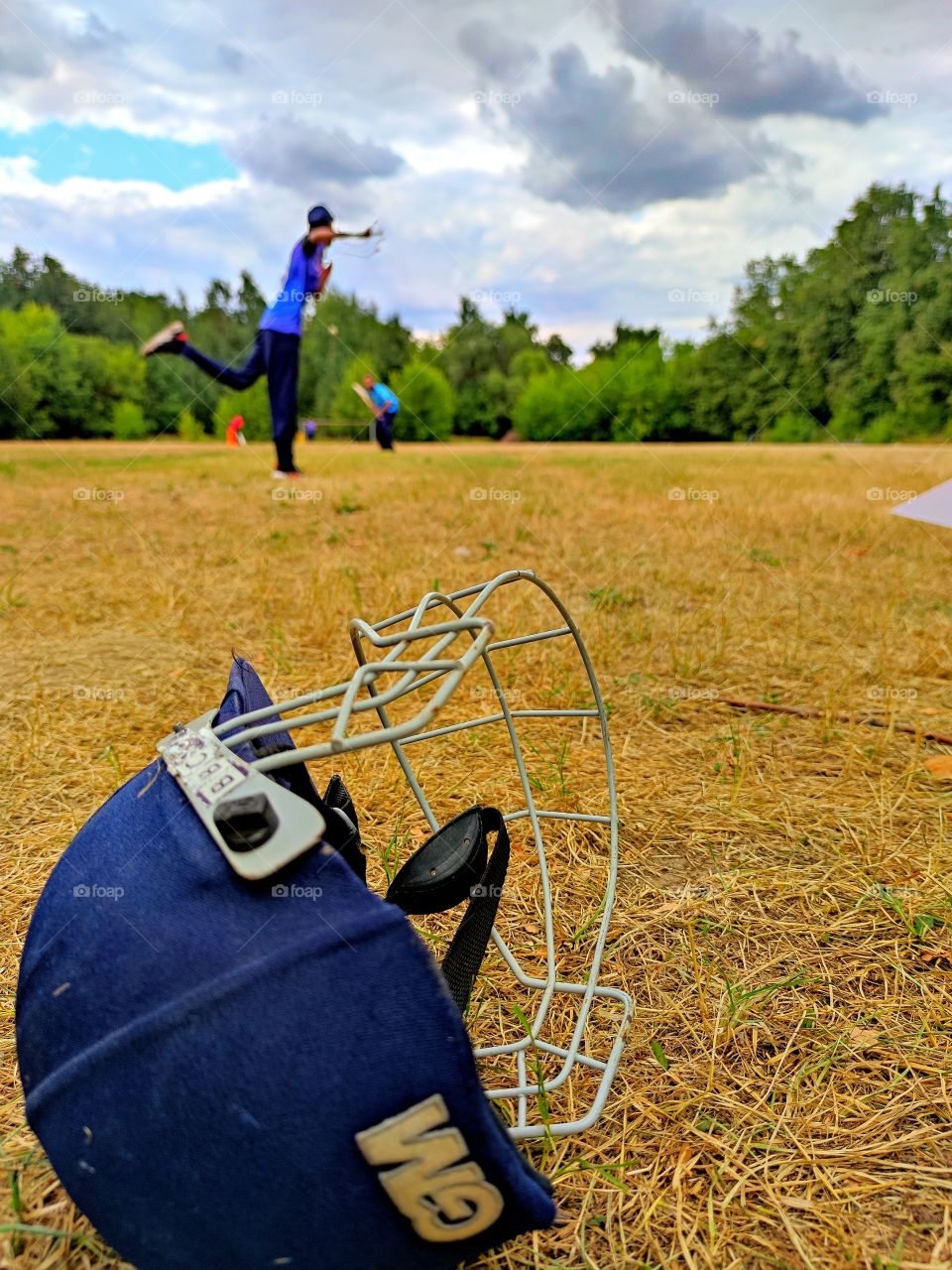 Field.  In the foreground, a protective helmet.  Cricketer field.