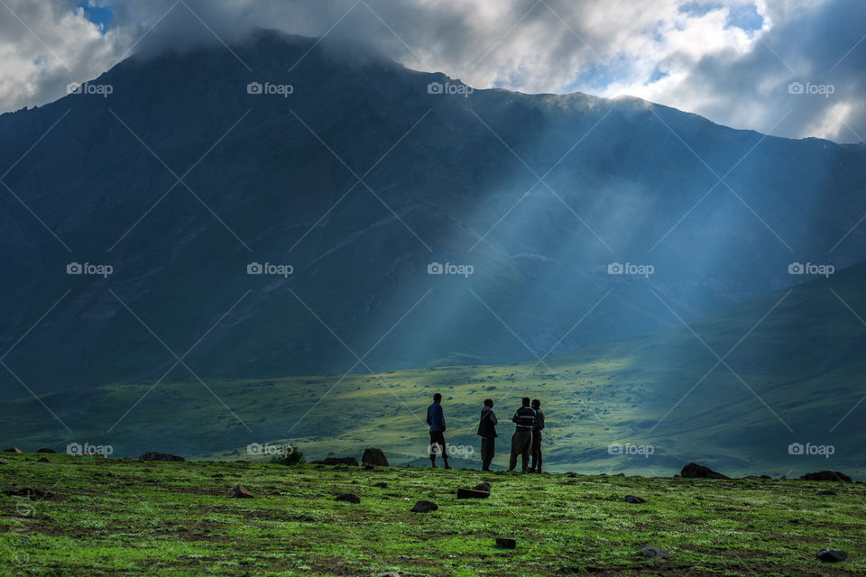 sun rays falling on group of men standing on a grassland over mountains