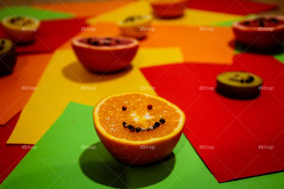 Explosion of colors and joy! This smiling orange, decorated with peppercorns, brings a touch of creativity and positive energy on a background full of vibrant shades.