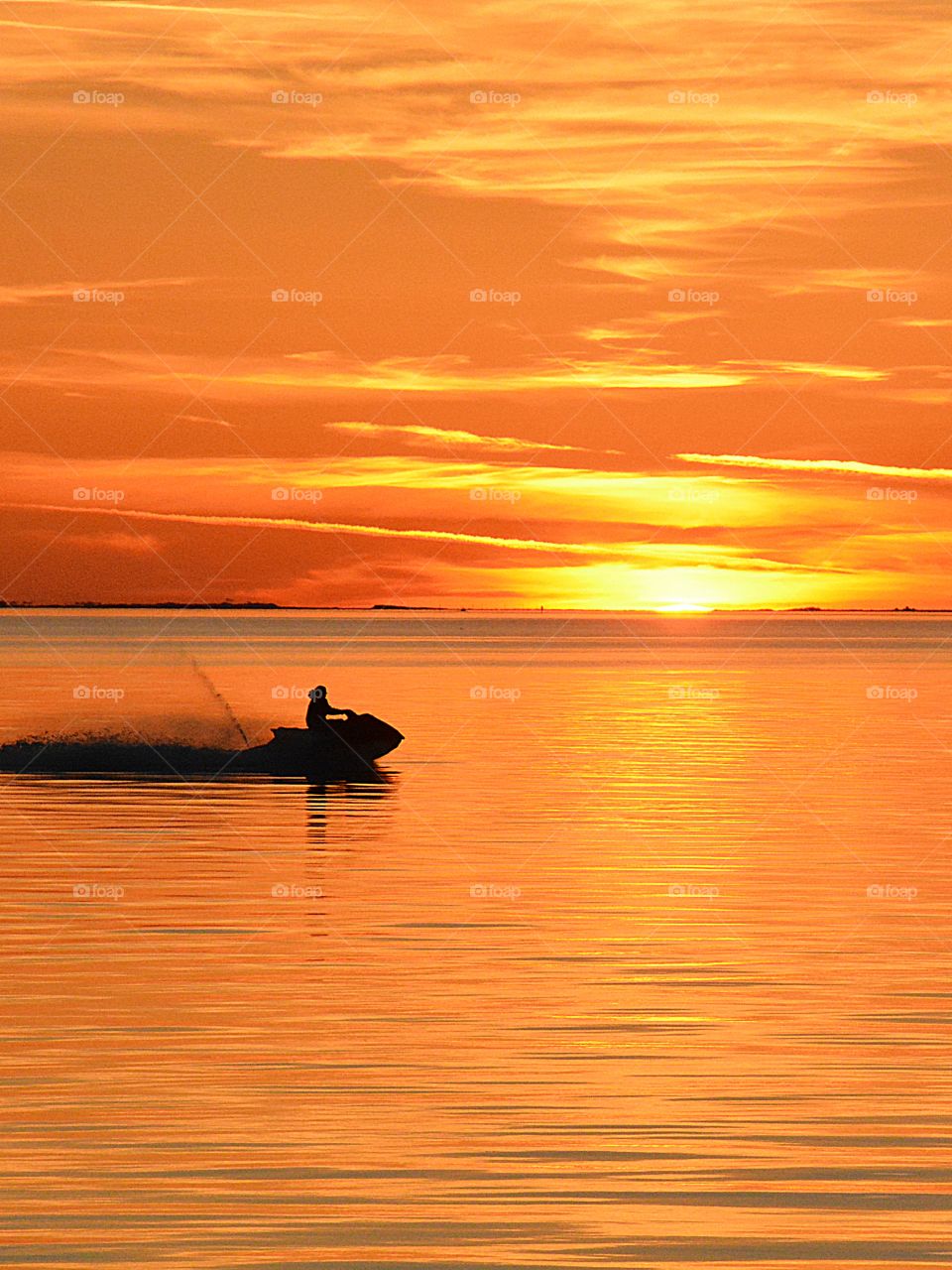 Sunrises and sunsets of USA - A man propels his wave runner across the surface of the bay engulfed in a magnificent golden sunset