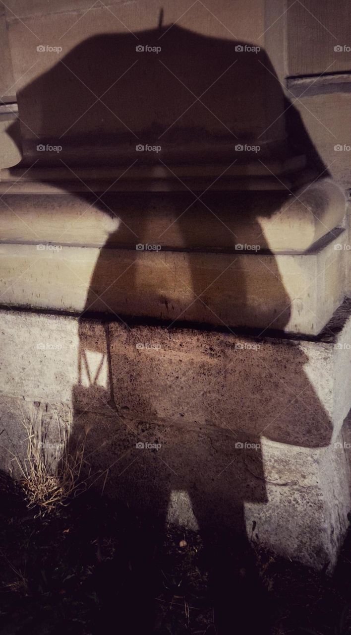 Shadow of a woman with an umbrella at night on the wall of a historic building.