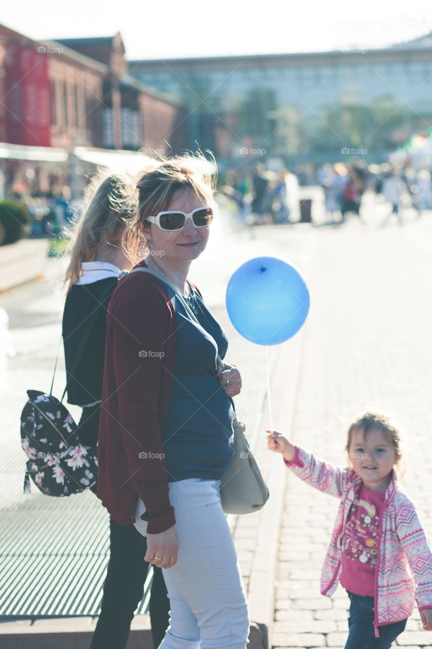 Mother walking with her daughters, spending time in center of city outdoors. Little girl holding blue balloon