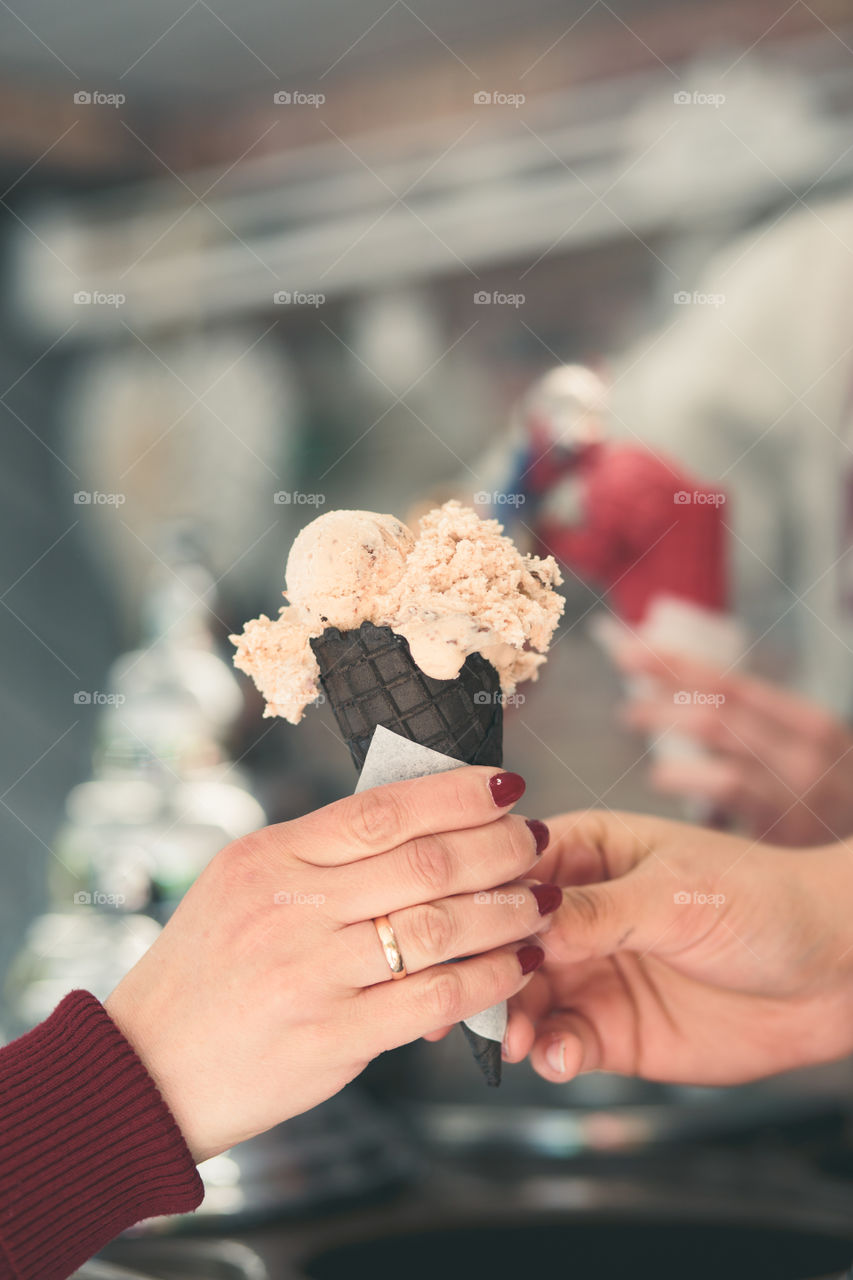 Woman buying couple scoops of  ice cream in a candy shop by a street. Woman putting a scoops of ice cream to a cones