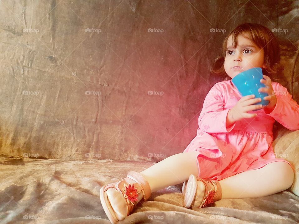 beautiful two year old model on silver couch with bright blue cup and pink dress