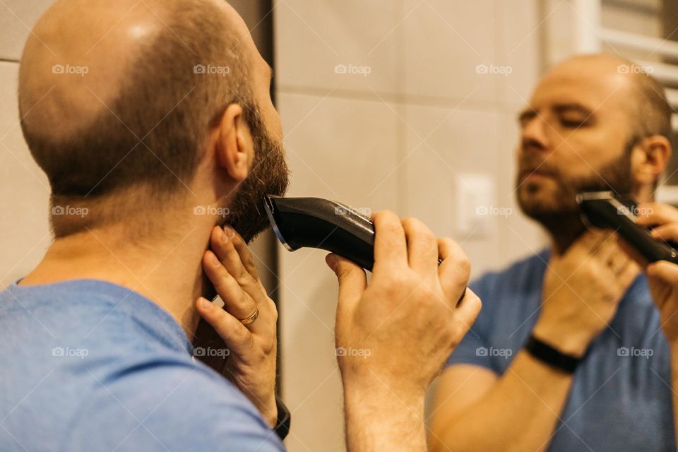 Millennial man using razor for shaving his beard.