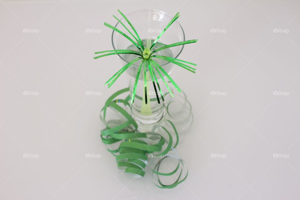 Glass with festive green straw and serpentine, white background 