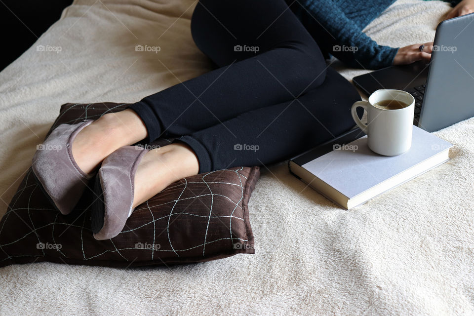 Young woman relaxing on her bed while working on her laptop