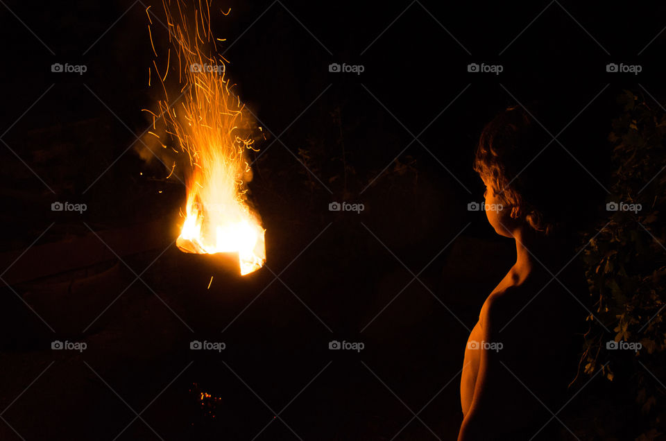 Silhoutte Of A Boy Standing In Front Of Flame On The Dark Background