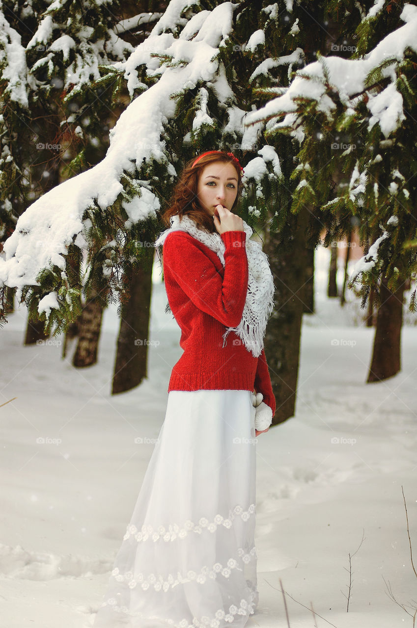 Winter portrait of young redhead woman in red sweater in snowcovered winter park.