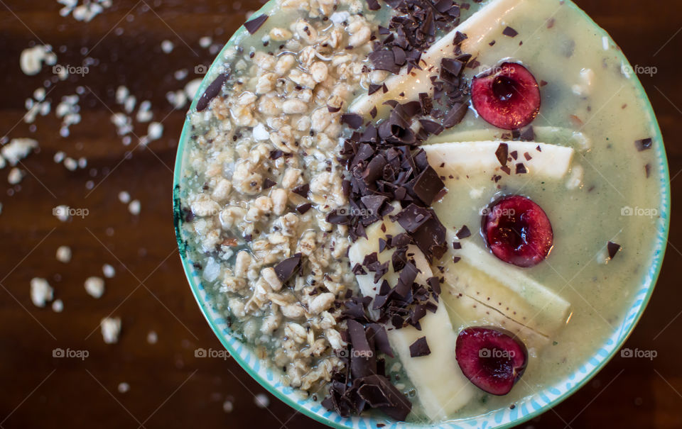 Chocolate banana and cherry with granola and coconut fresh fruit smoothie bowl decorated with sliced fruit from high angle view. Artisanal healthy eating food photography background 