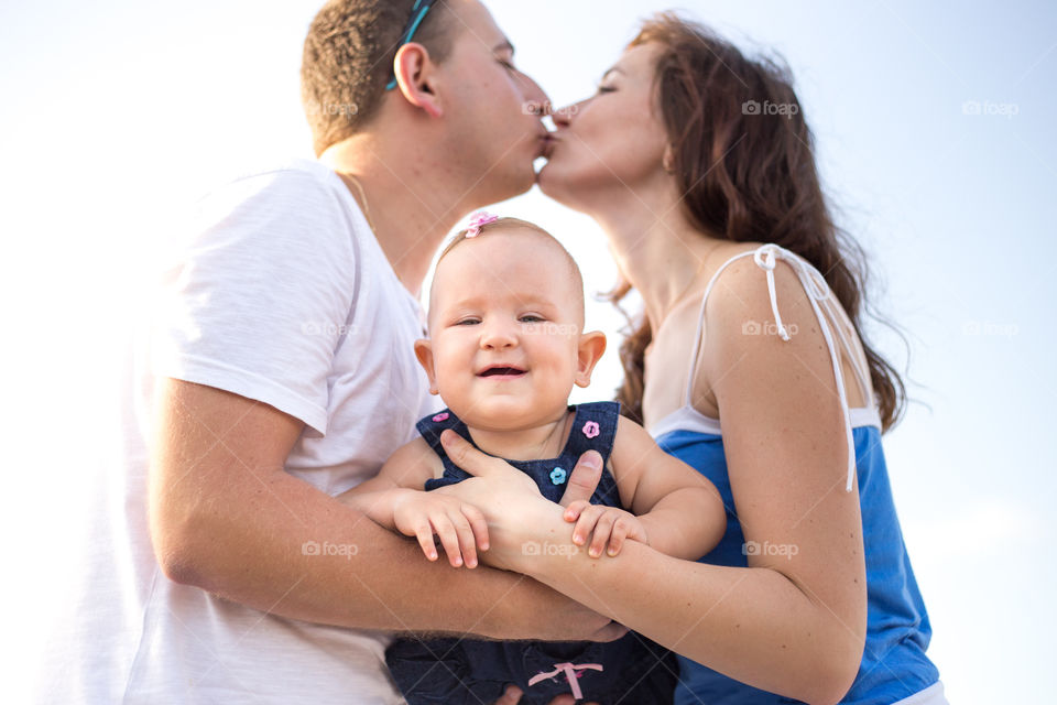 Kissing parents holding baby between them 