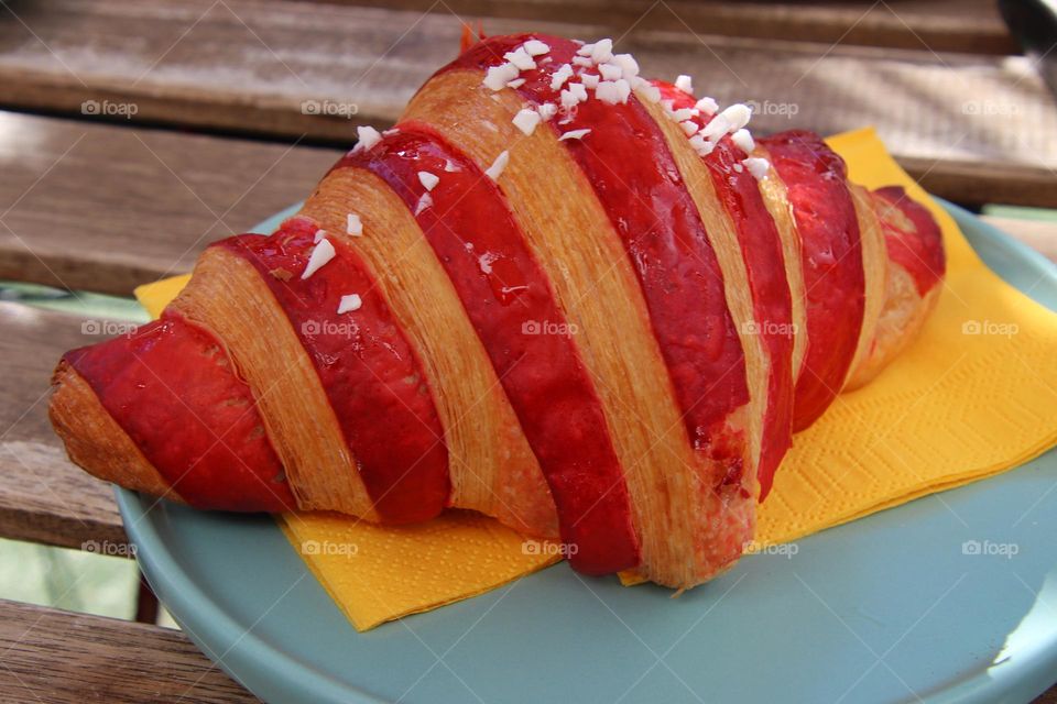 Close-up of a red brown striped croissant on blue plate with yellow napkin