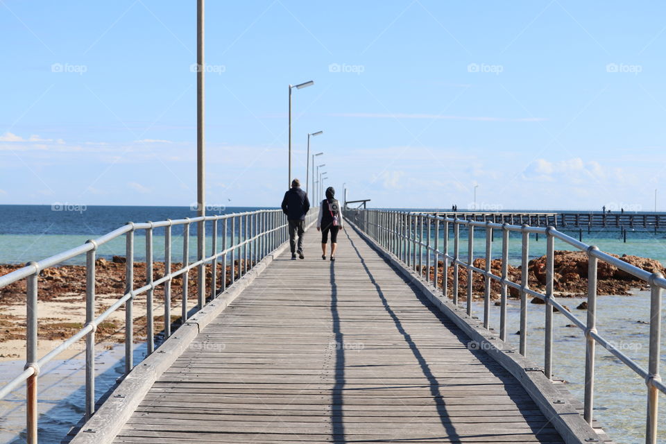 Mar female couple walking down public wharf Jetty Oceanside on sunny day
