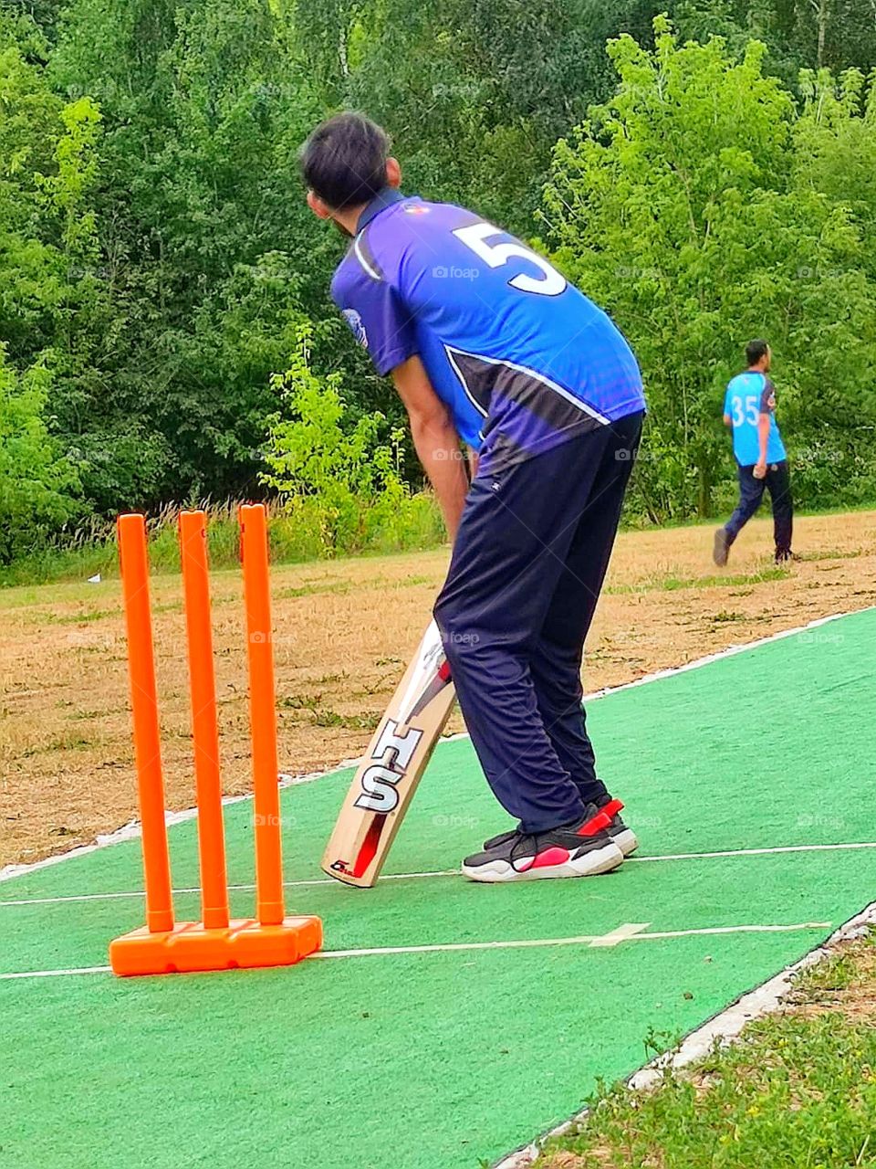 Cricket training.  A man in a blue uniform stands in a bat stand waiting for the ball