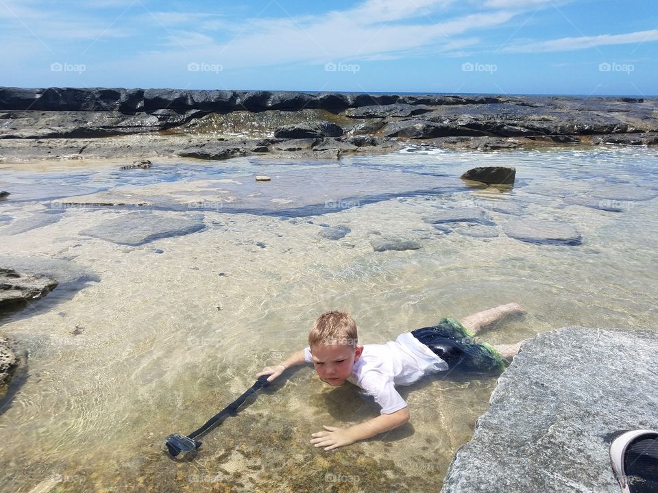 Boy swims in tidal pool, trying to catch gopro footage of fish