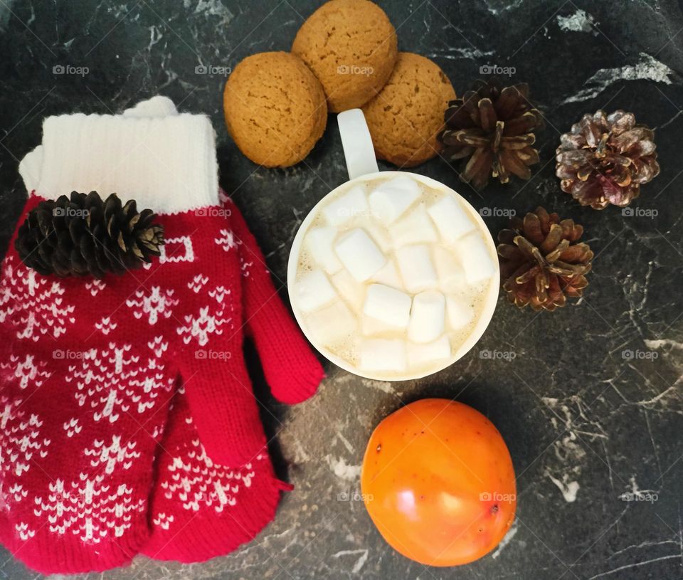 cappuccino, cones, mittens and persimmons on the table, winter mood, red bumps with white snowflakes, black background, coffee with milk, dark and cozy, coffee mug.