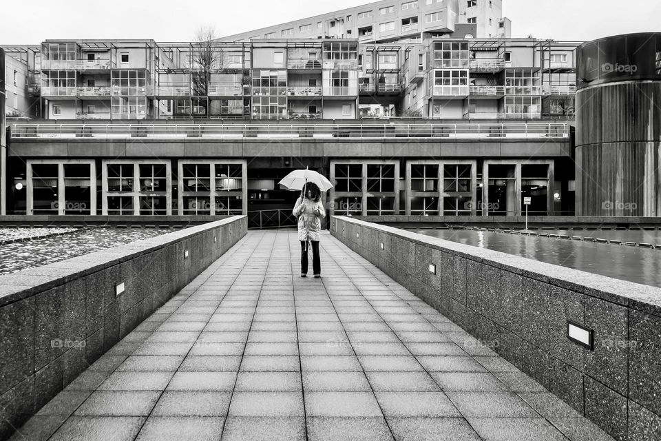 A person stands under an umbrella in front of modern housing apartments in Paris