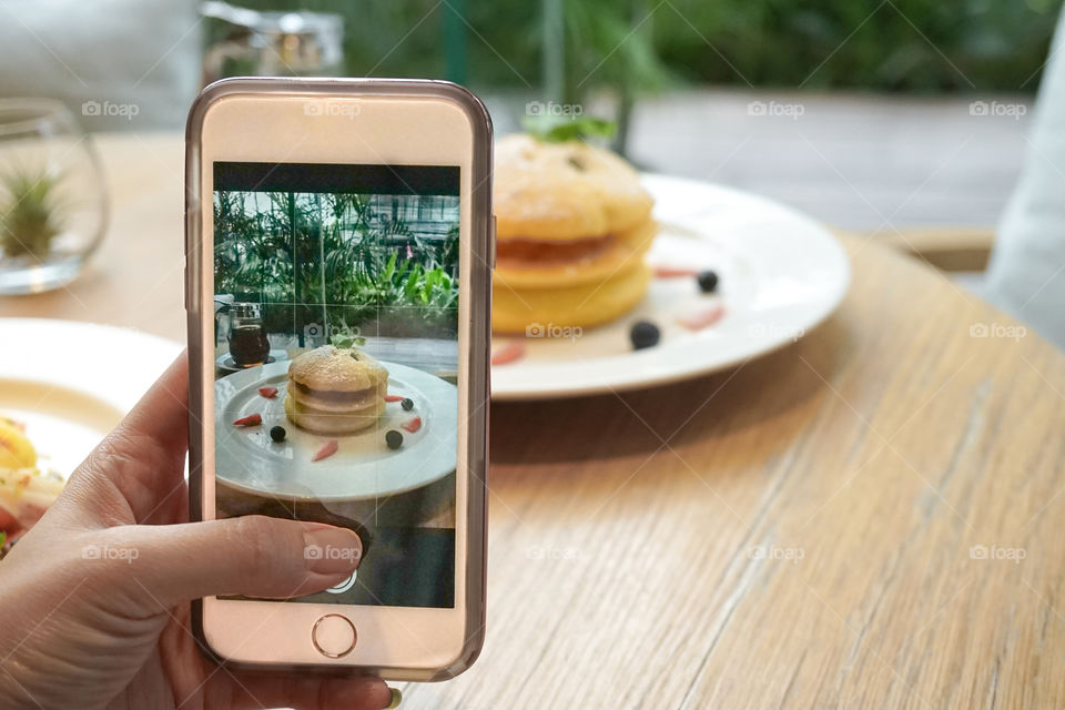 A hand holding a smart phone taking a photo of a pancake. Smartphone photography is now becoming a big trend and a change in photography industry.