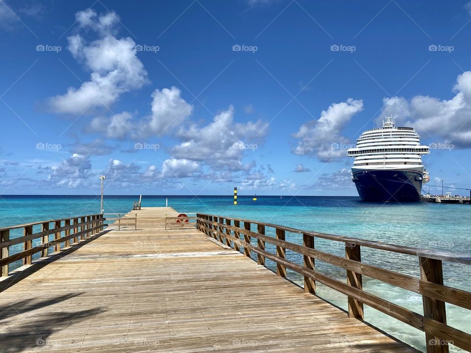 A wooden dock out over the water with a cruise ship in the background 