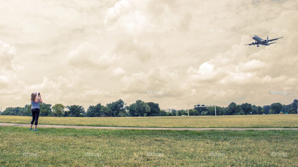 A woman uses her mobile device to photograph an airplane landing