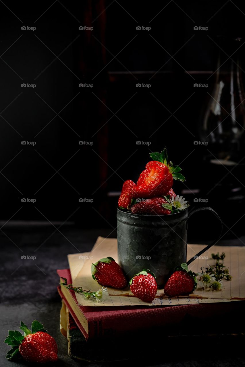 Red strawberries in the rustic iron mug with dark background.