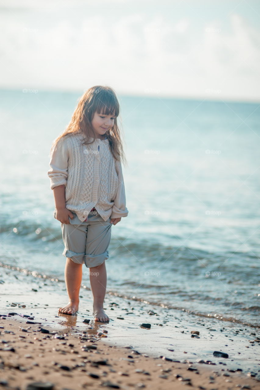 Little girl walking on the sea shore at sunny morning 