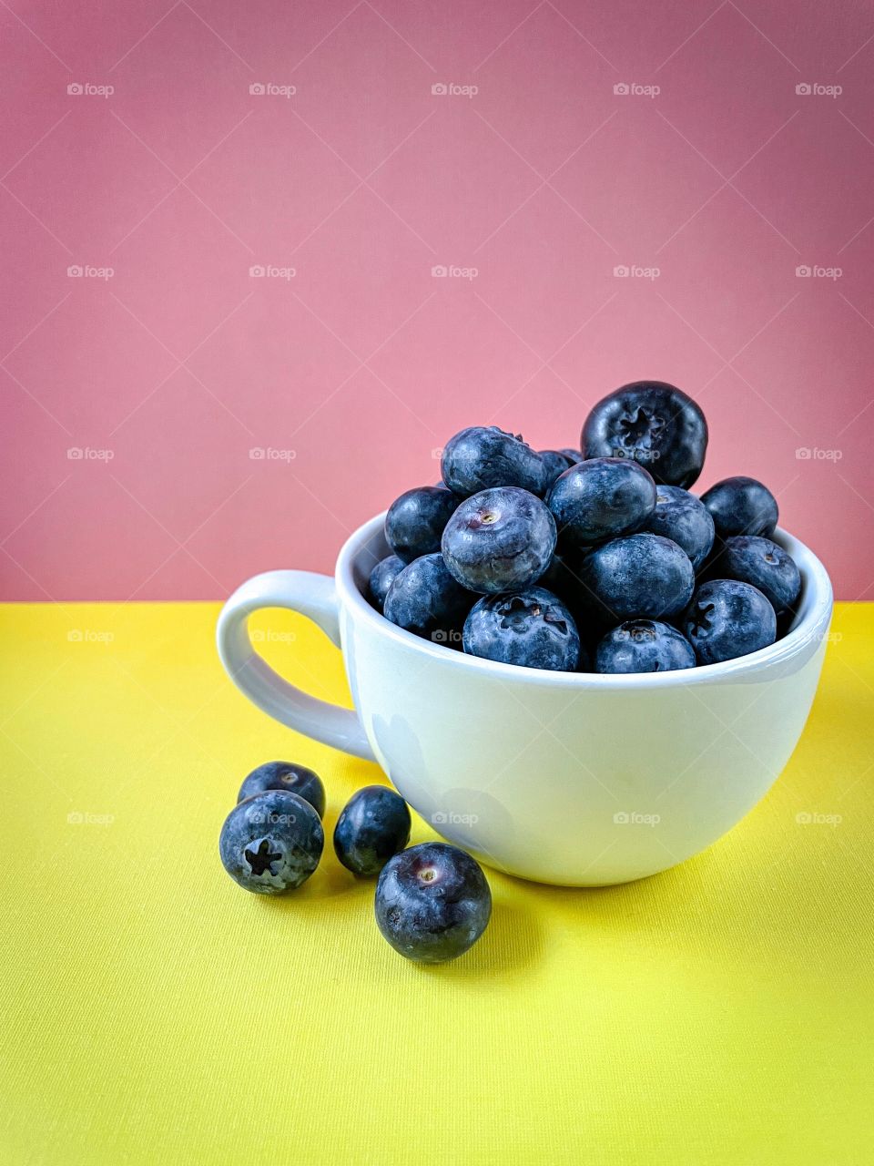 Bright and delicious blueberries in a white cup with a sunny and cheerful yellow and pink background. 