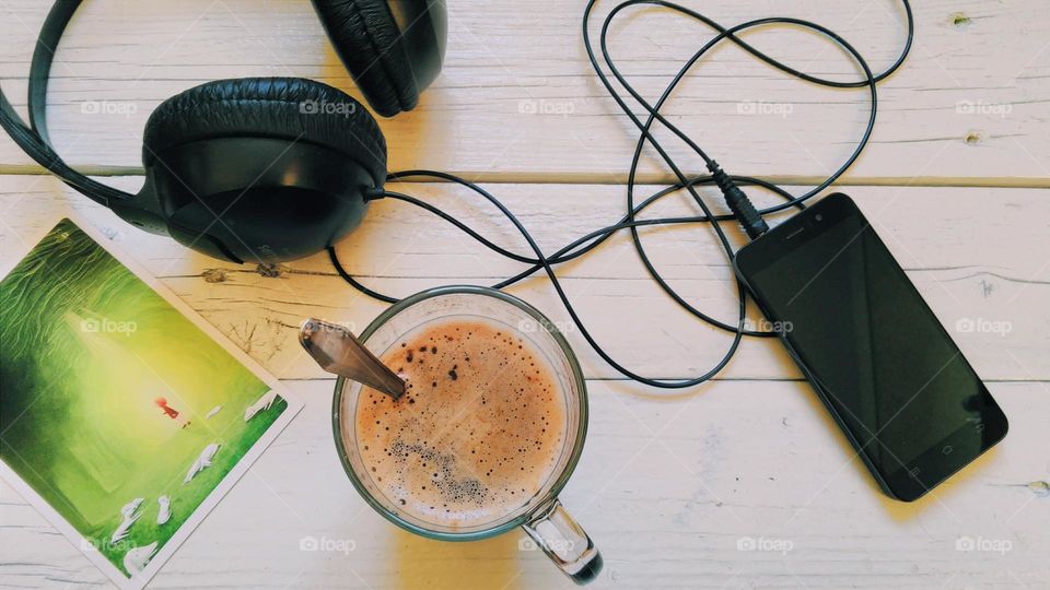 A cup of black coffee, a smartphone, headphones and a postcard are waiting for you