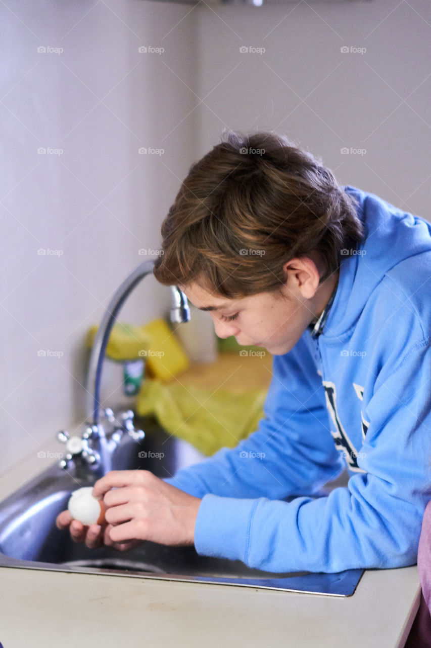 Boy peeling brown egg in kitchen