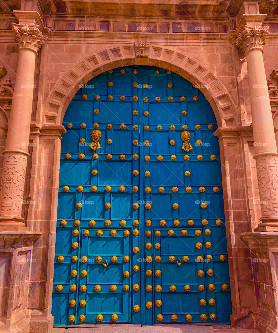 A beautiful large blue door contrasts against the orange building and the golden studs embedded in the door