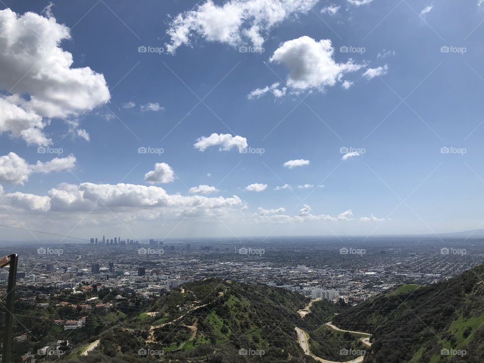 Viewing the city from a mountain where trails, mountains, foliage, clouds and Los Angeles city can be seen. 