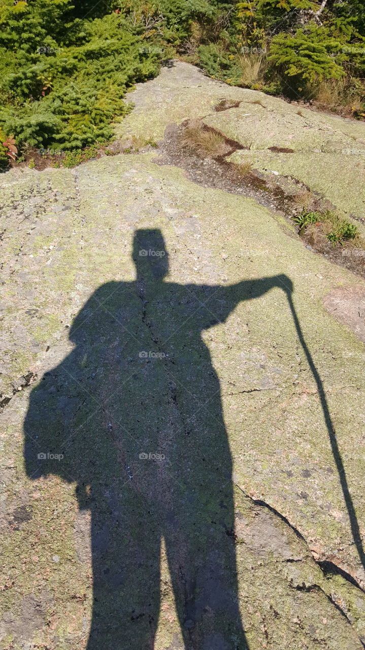 A hiker marks their shadow as the sun passes over them and over the top of the mountain.