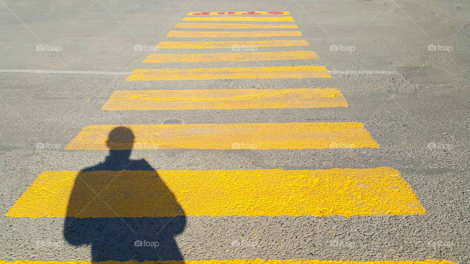 a person stands at the beginning of a pedestrian crossing, where it is written stop and waits for the passage time, on the yellow lines drawn on the asphalt, the shadow of a person is clearly visible, copy space for text