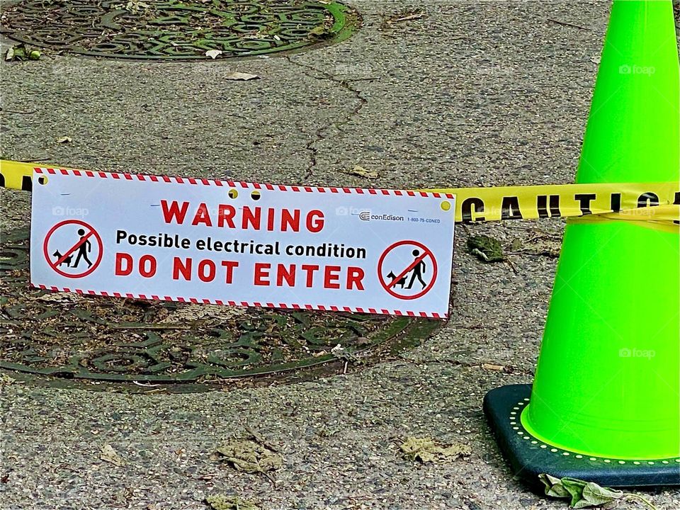„WARNING - DO NOT ENTER“ says the sign tied to the fluorescent yellow sectioning tape wound around neon green plastic poles to designate the area to be kept clear. 2022. Hypnotic Productions
